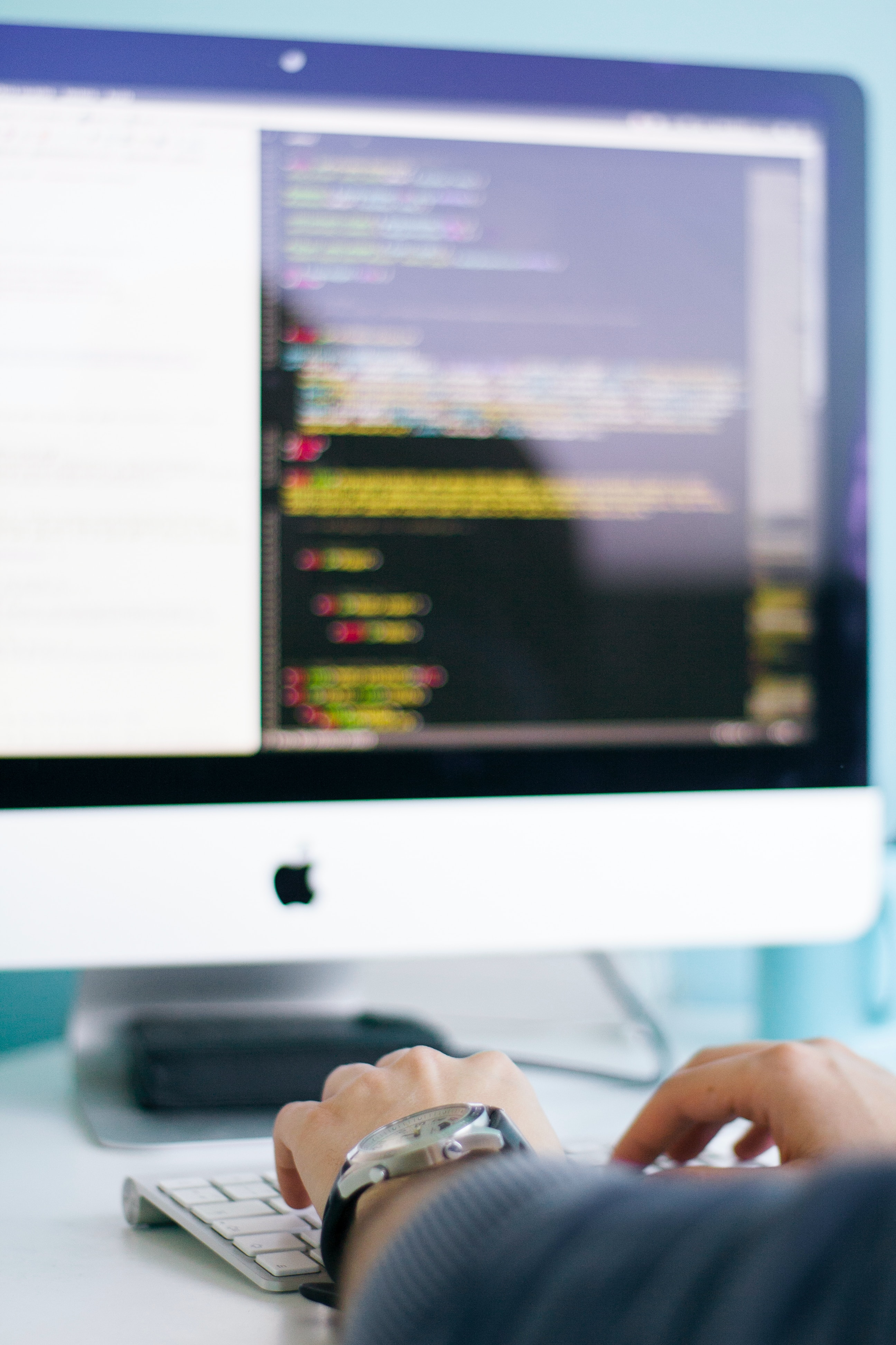 office worker typing at a mac, code is on the screen